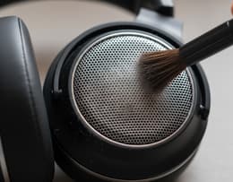 Soft-bristled brush sweeping dust from a headphone speaker grille.